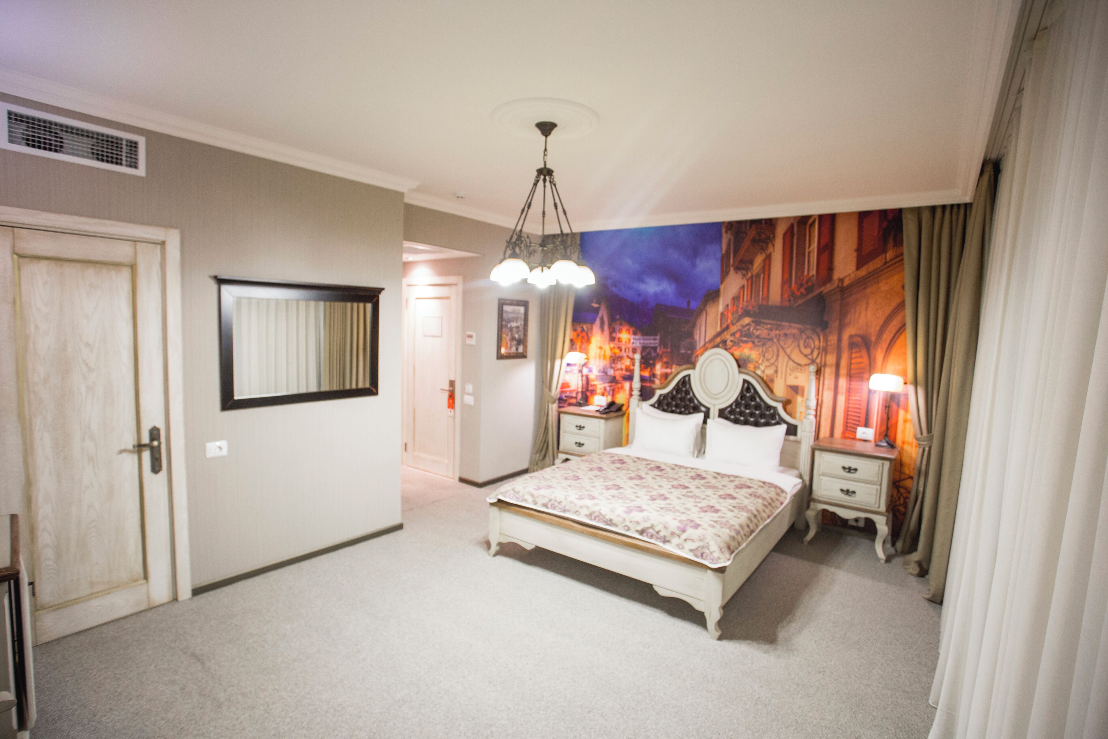 Un dormitorio con cama, mesitas de noche, un espejo y un mural en la pared.