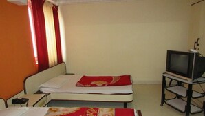 A room with two beds, a television on a stand, and a window with curtains. - Hotel Sheela International (Durg)