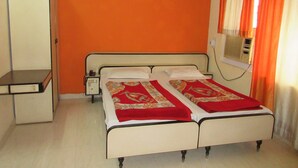 Cama doble con colcha roja y beige, mesita de noche, armario y equipo de aire acondicionado.
