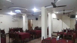 A dining area with tables covered in red tablecloths, wooden chairs, and ceiling fans. - Hotel Sheela International (Durg)