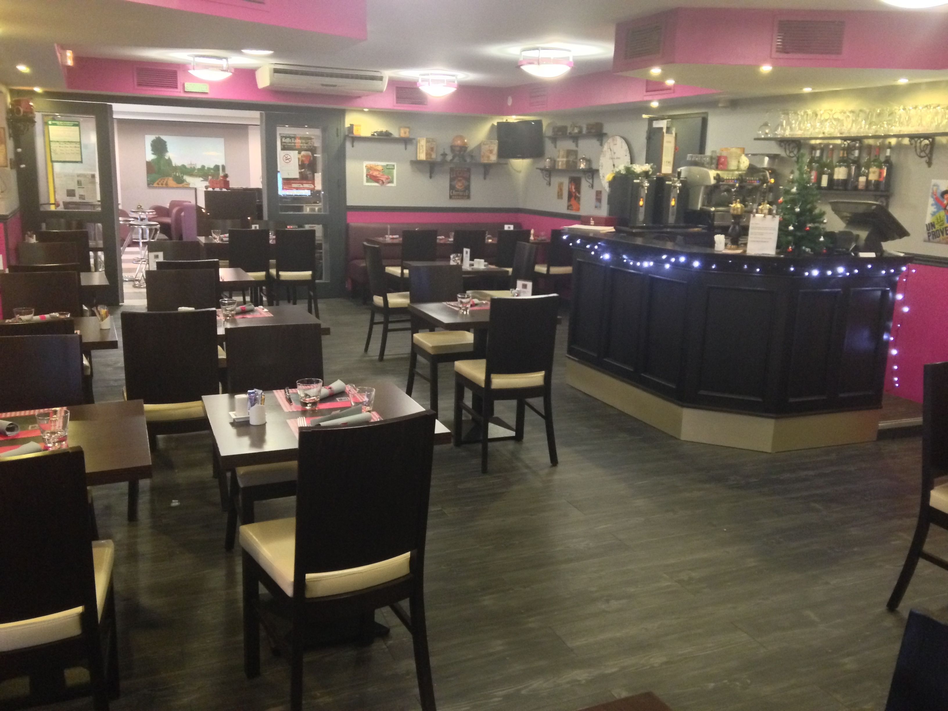 Interior de restaurante con mesas y sillas, una zona de bar con mostrador, y una pared con varias decoraciones y un reloj.