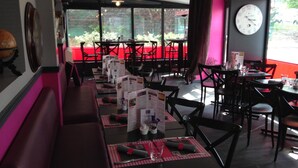 Un restaurante con mesas largas, sillas negras y rojas, y soportes para menús.