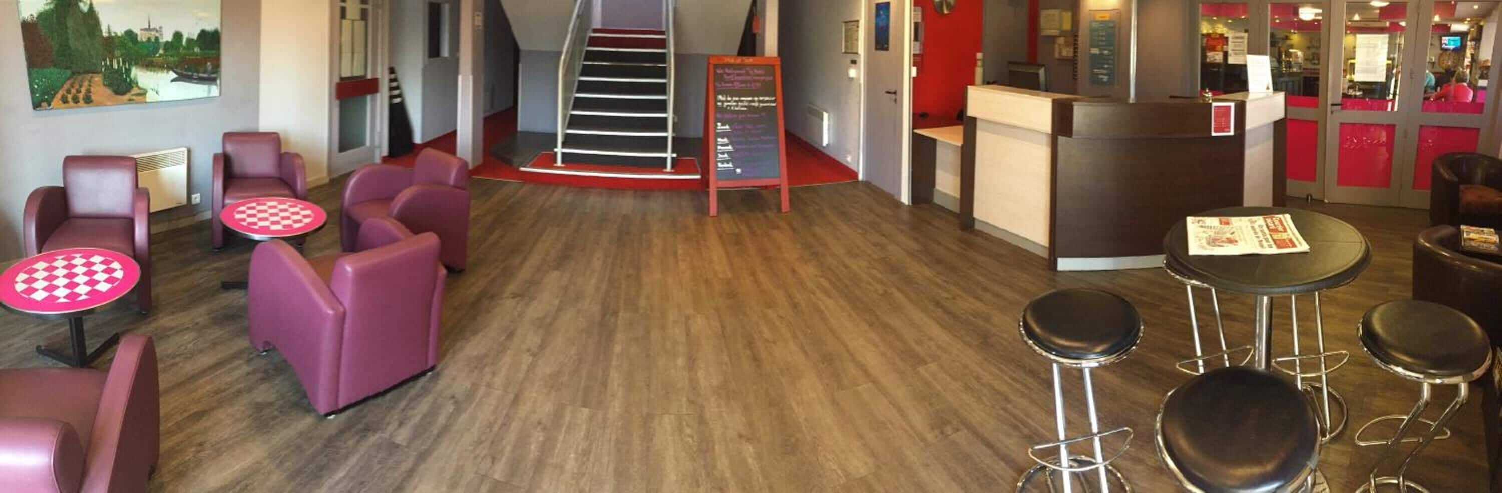 Un vestíbul d'hotel amb taula de pissos, seients de color morat, una escala i una recepció.