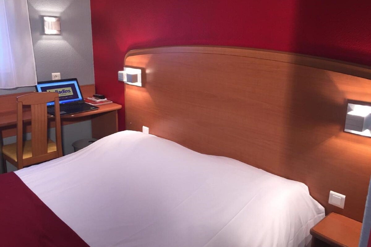 Una habitación de hotel con cama, escritorio, laptop, silla y mesita de noche.