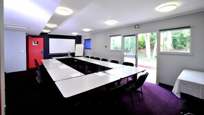 Un salón de conferencias con una larga mesa, sillas, una pizarra y una pantalla de proyector.