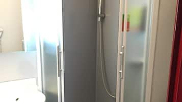 Eine Duschkabine mit Glas, ein weißes Waschbecken und ein Handtuch auf dem Boden.