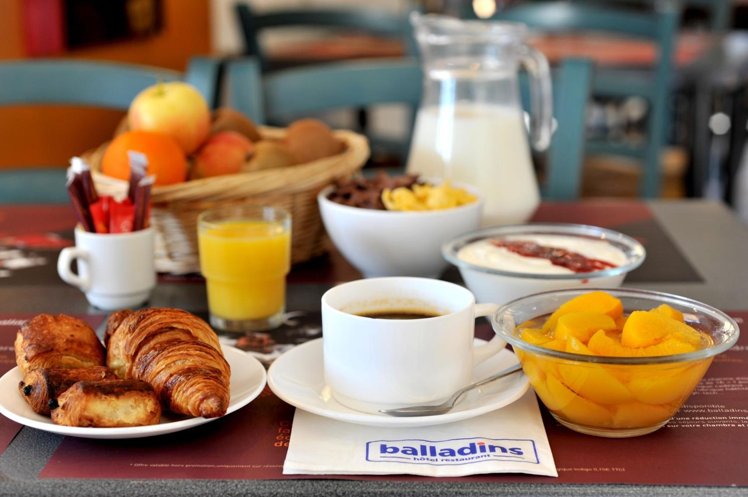 Ein Frühstückstisch mit Croissants, Orangensaft, Kaffee und einer Obstschale.
