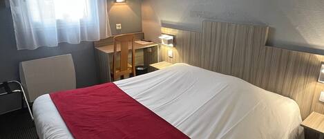 Una habitación de hotel con una cama grande, un escritorio, una silla y un ventanal con cortinas.