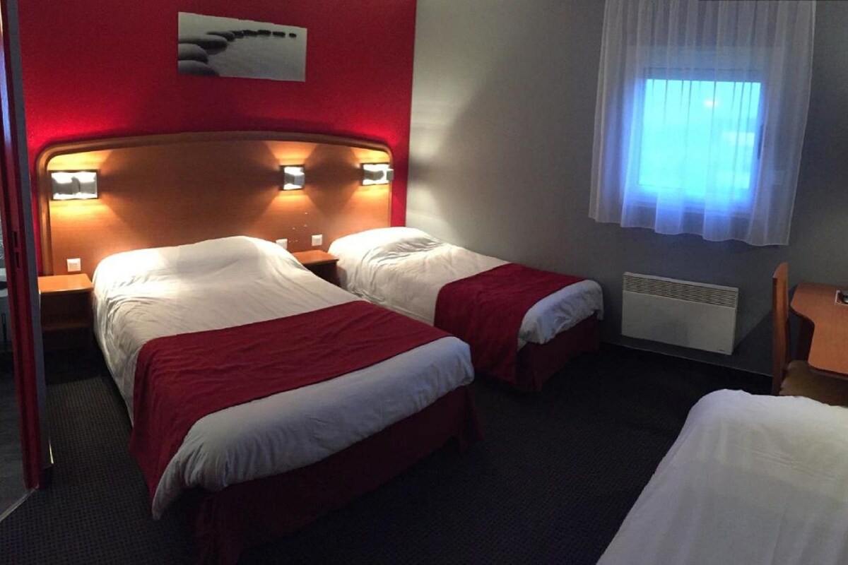Ein Hotelzimmer mit zwei Betten, einer roten Wand, einem Fenster mit weißen Vorhängen und einer Wandleuchte.