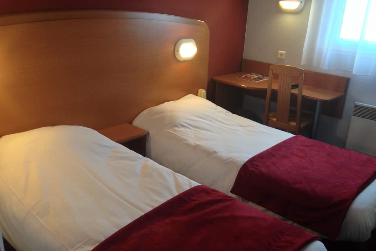 Una habitación de hotel con dos camas, cabecera de madera, una mesita y una silla.