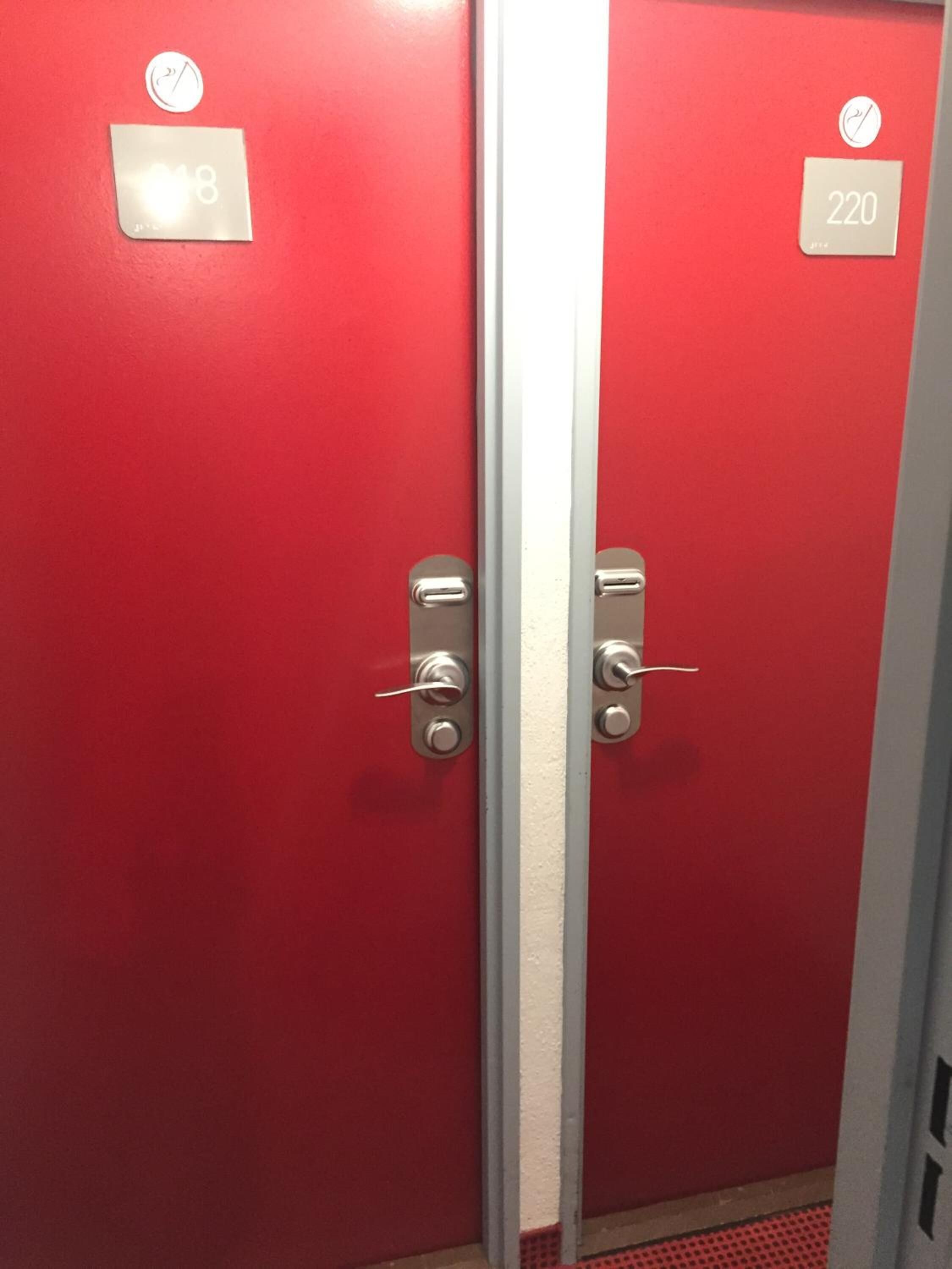 Zwei rote Türen mit den Nummern 018 und 220, jeweils mit einem kleinen, runden Logo darüber.