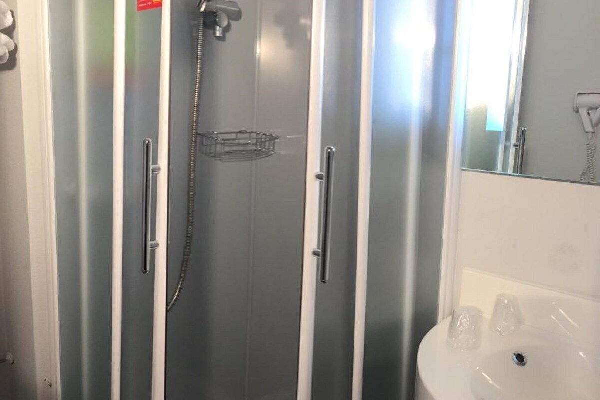 Un baño con ducha envuelta en vidrio, un lavamanos blanco y un espejo sobre él.
