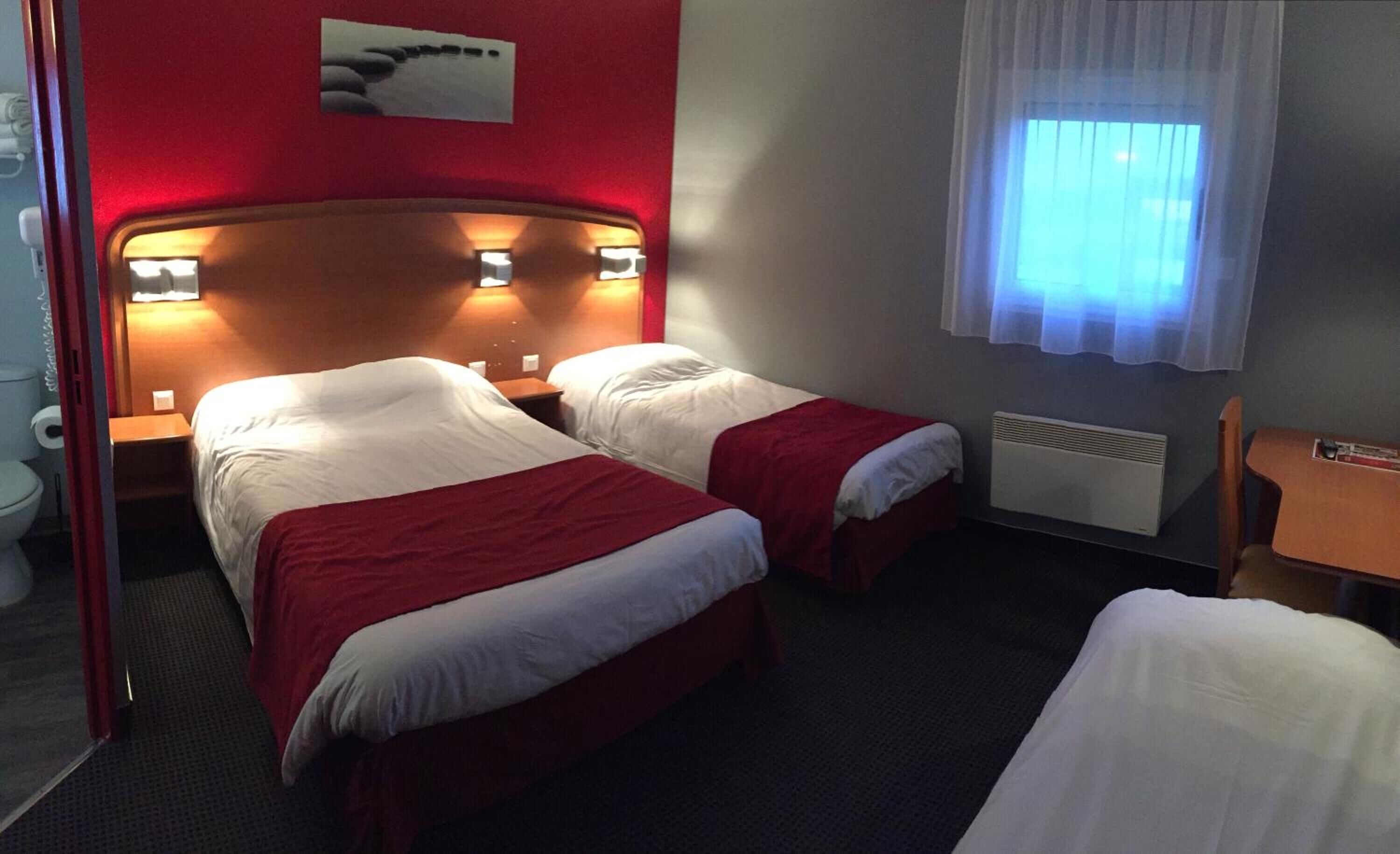 A hotel room with two beds, a red wall, a window with sheer curtains, and a radiator.