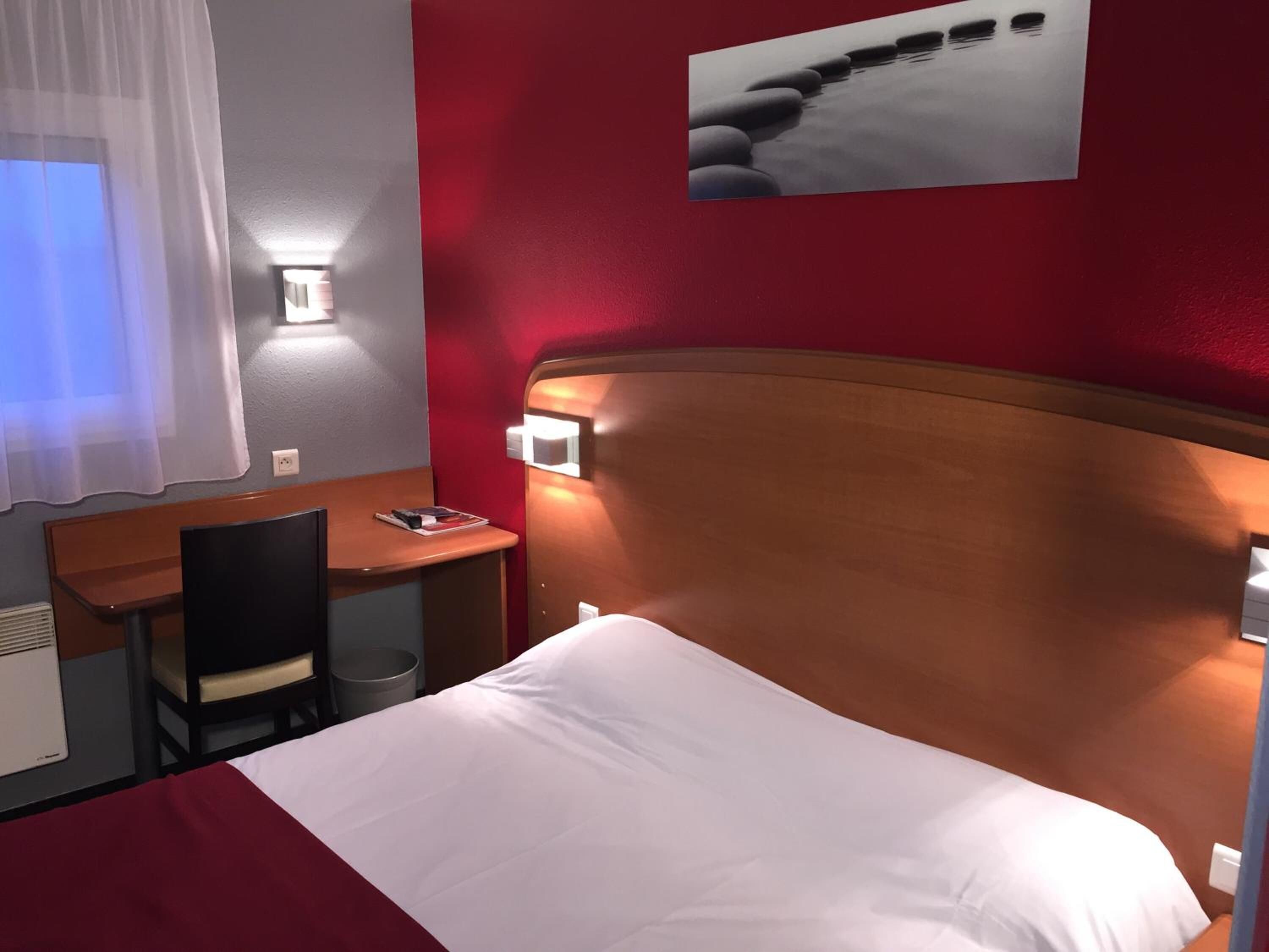 Una habitación de hotel con cama, escritorio, silla y luz empotrada en la pared.