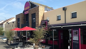 Un área de estar al aire libre con mesas y sombrillas rojas, un edificio de ladrillo con el letrero 'Balladins' y un letrero que indica 'BISTRO', un restaurante.