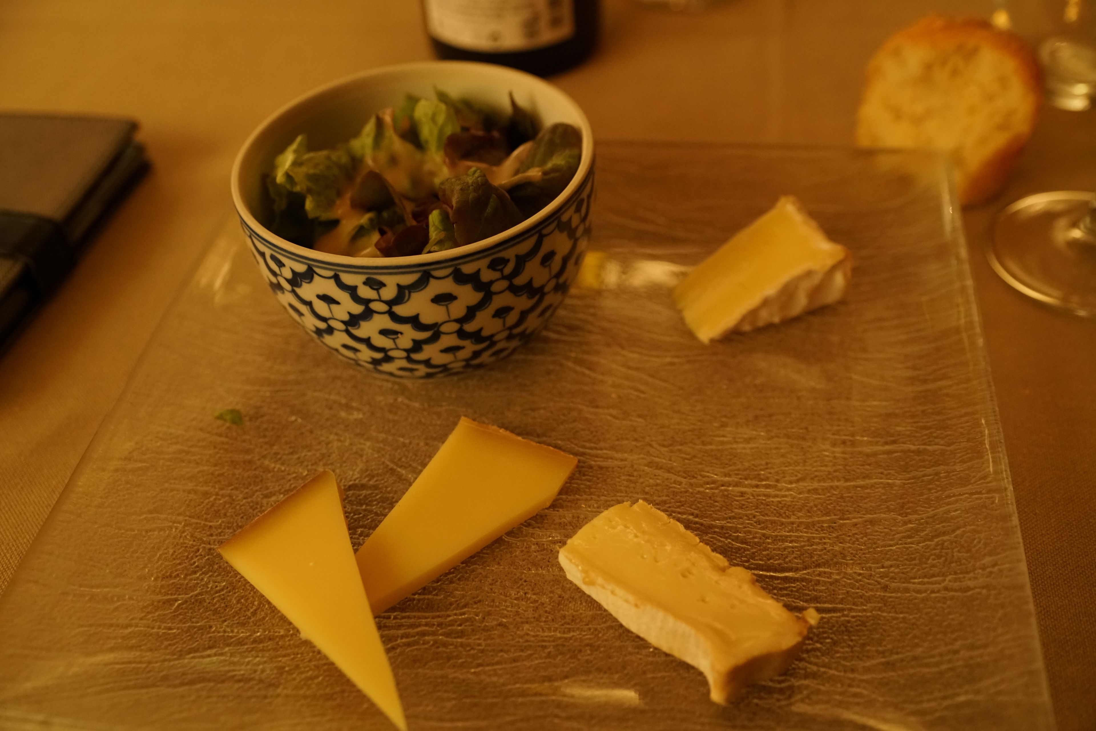 A table with a bowl of salad, two pieces of cheese, and a slice of bread.