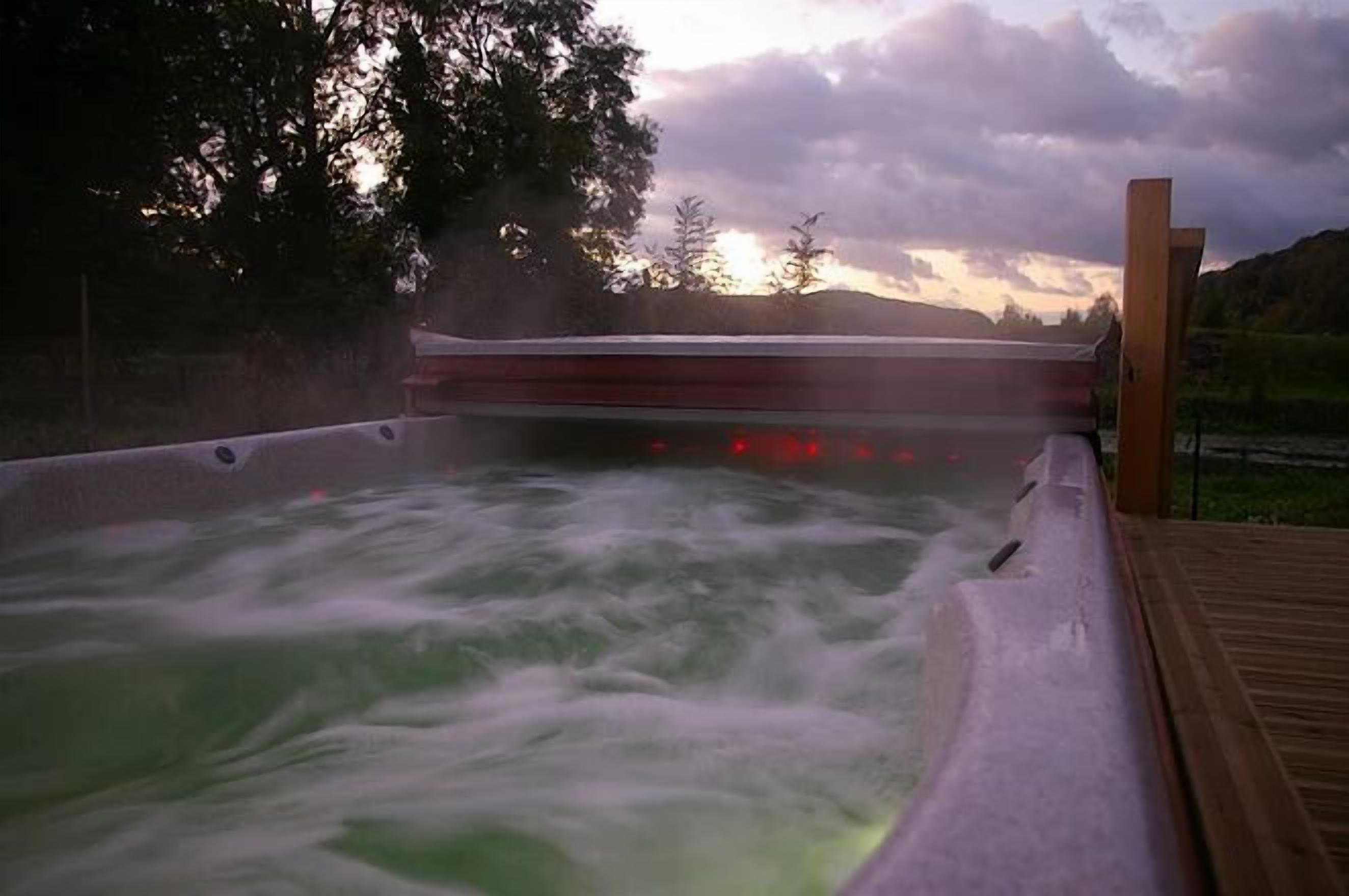 A hot tub with a wooden deck and a view of trees and hills in the background.