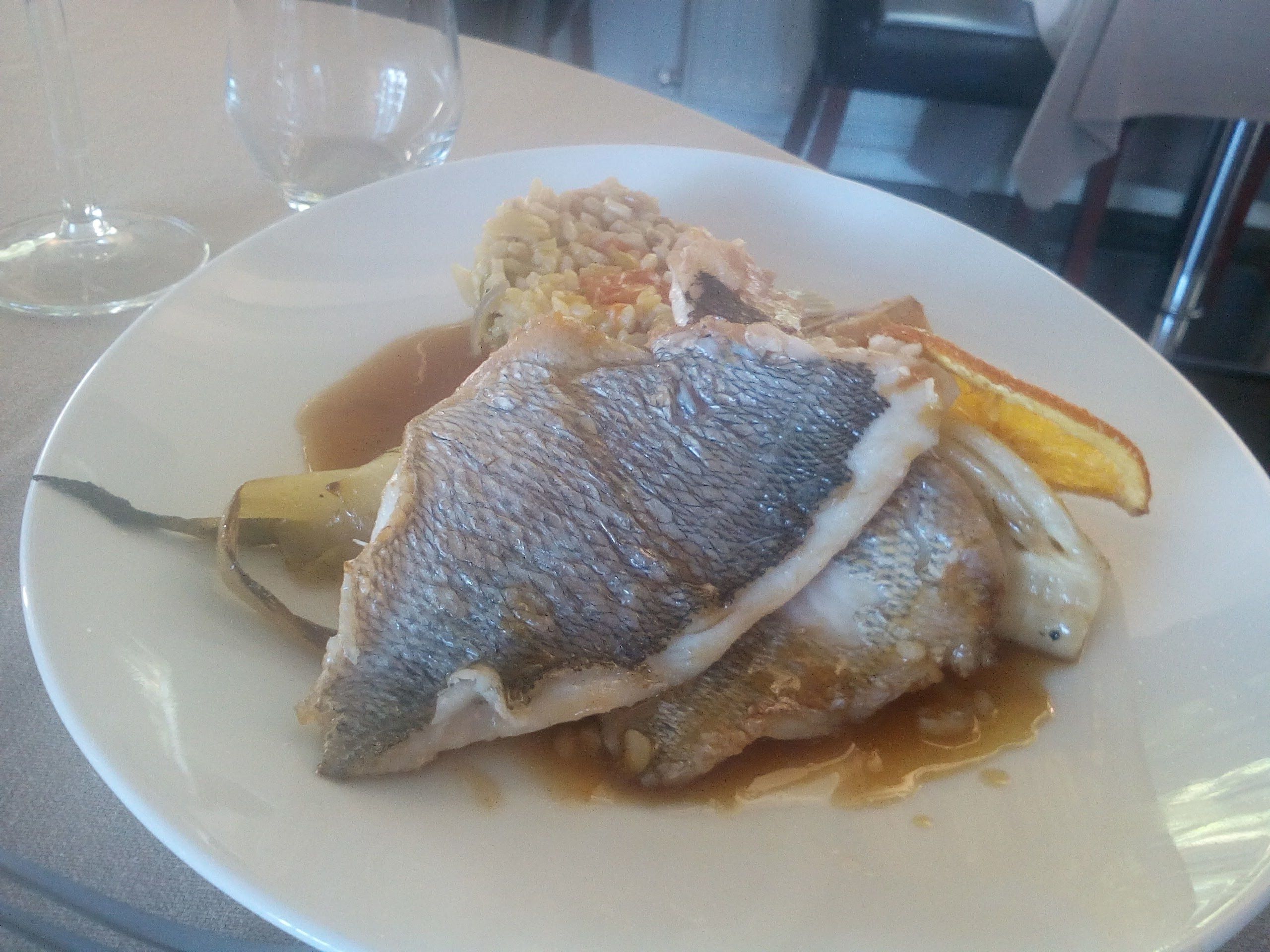 A plate with fish, rice, and a slice of orange on a table.