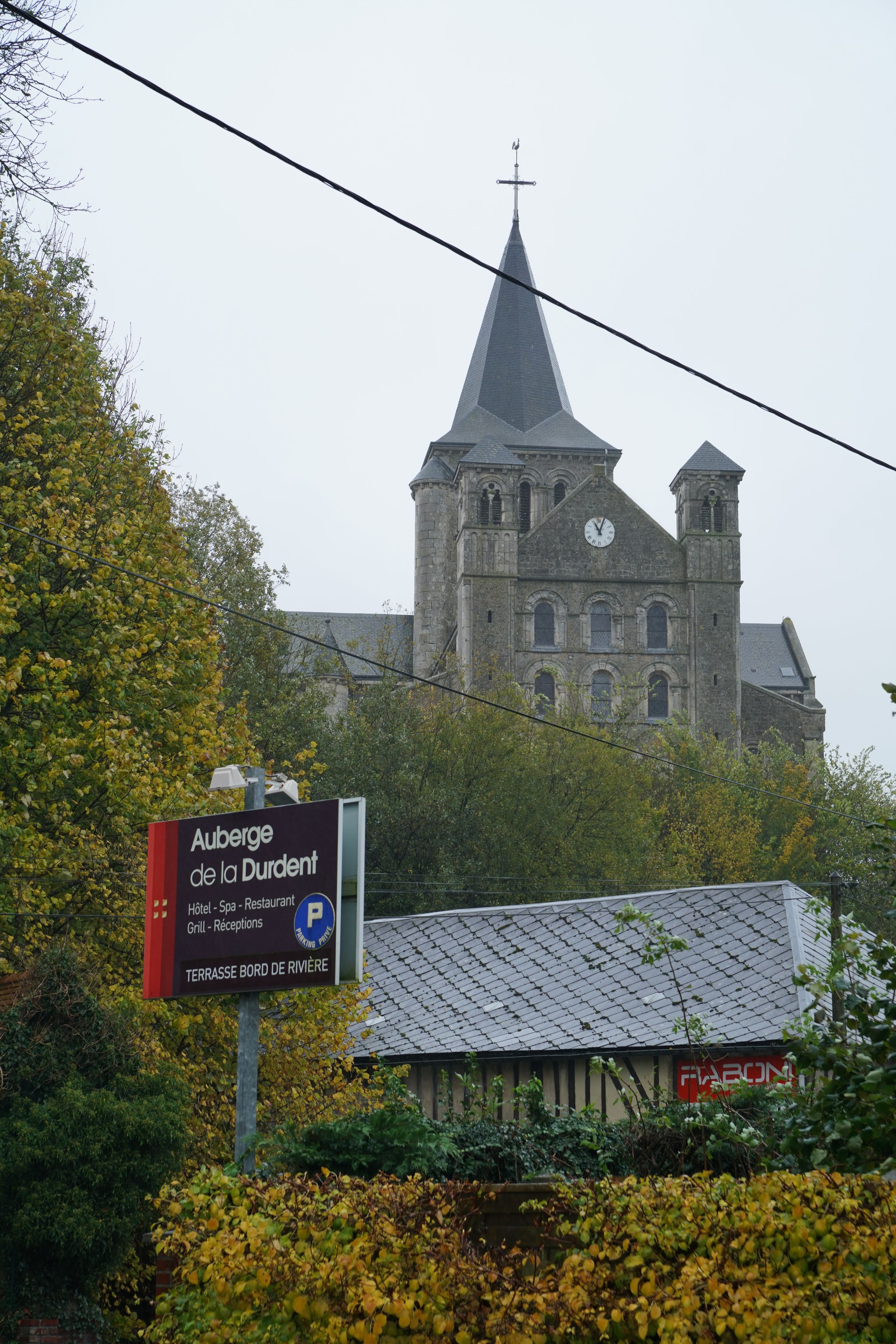 A church with a clock tower and a sign for Auberge de la Durdent.