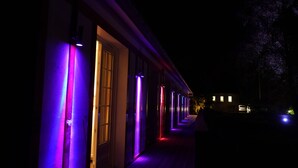 Un pasillo con líneas verticales iluminadas, un suelo de madera y un edificio al fondo.