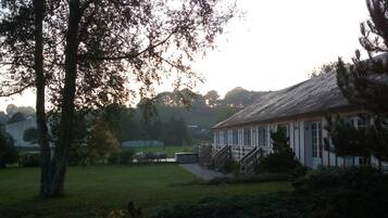 A building with a porch and steps, surrounded by greenery and a grassy area.