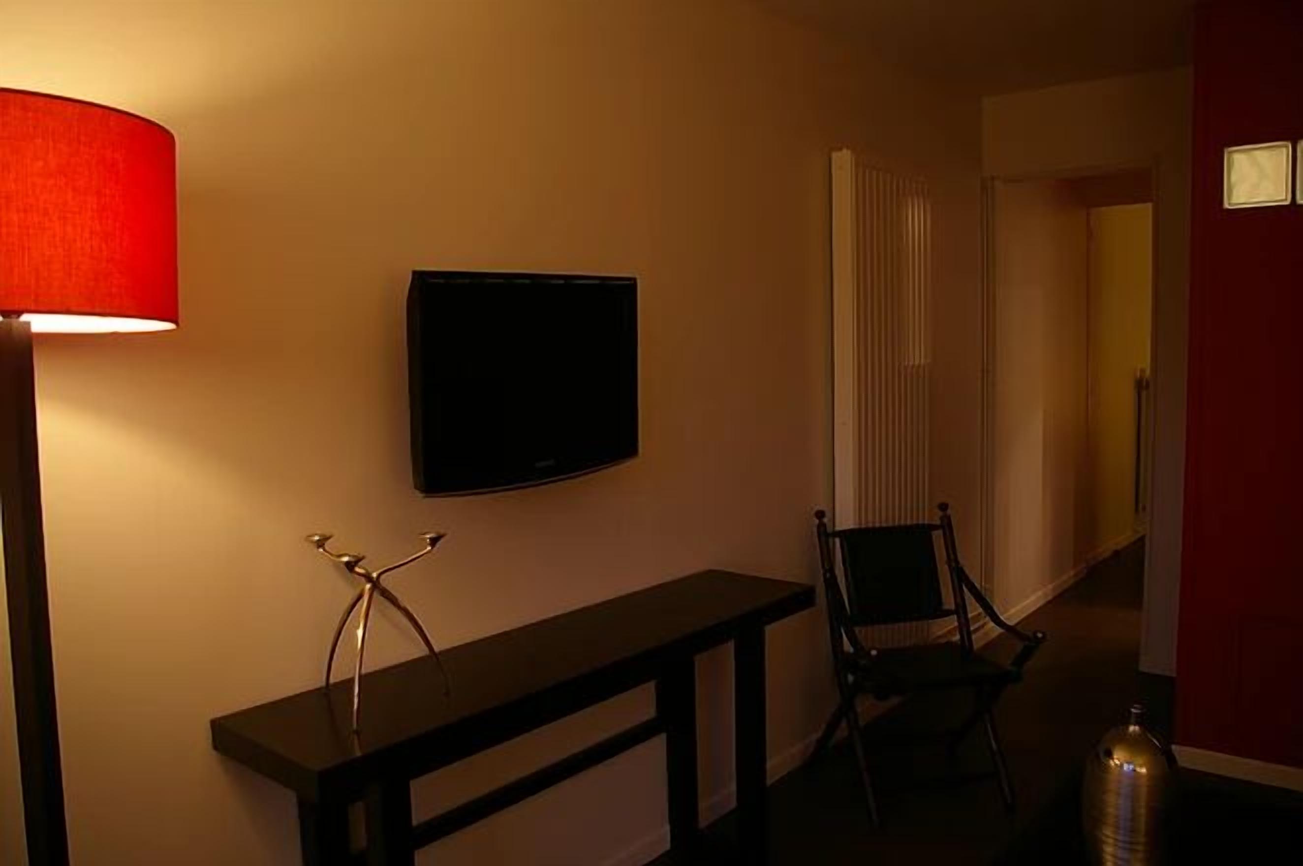 A hallway with a TV mounted on the wall, a bench, and a chair.
