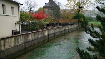 A riverside walkway with outdoor seating, a stone wall, and a building in the background.