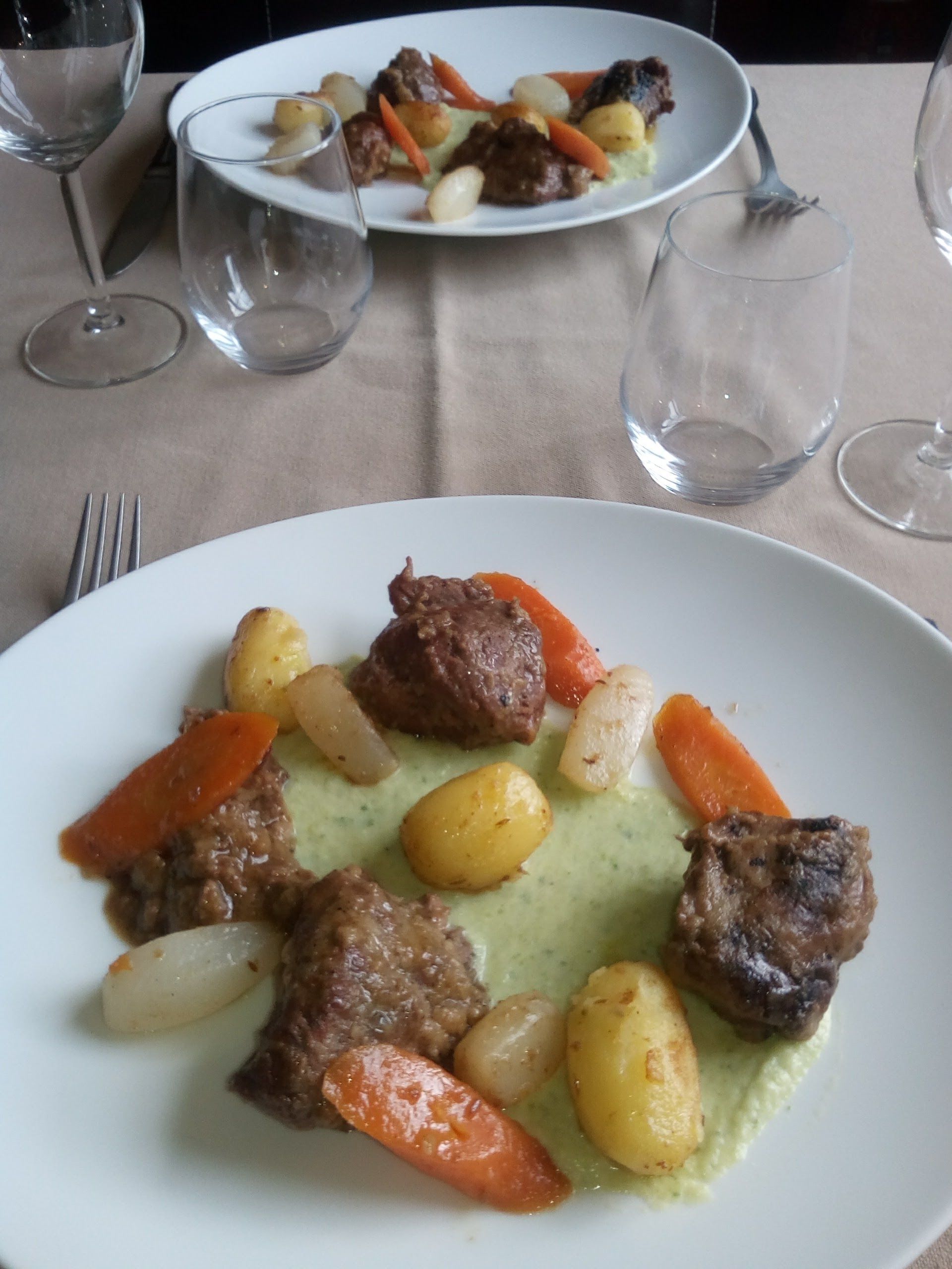 Una mesa de comedor con un plato de estofado de carne y verduras, un tenedor y copas de vino vacías.