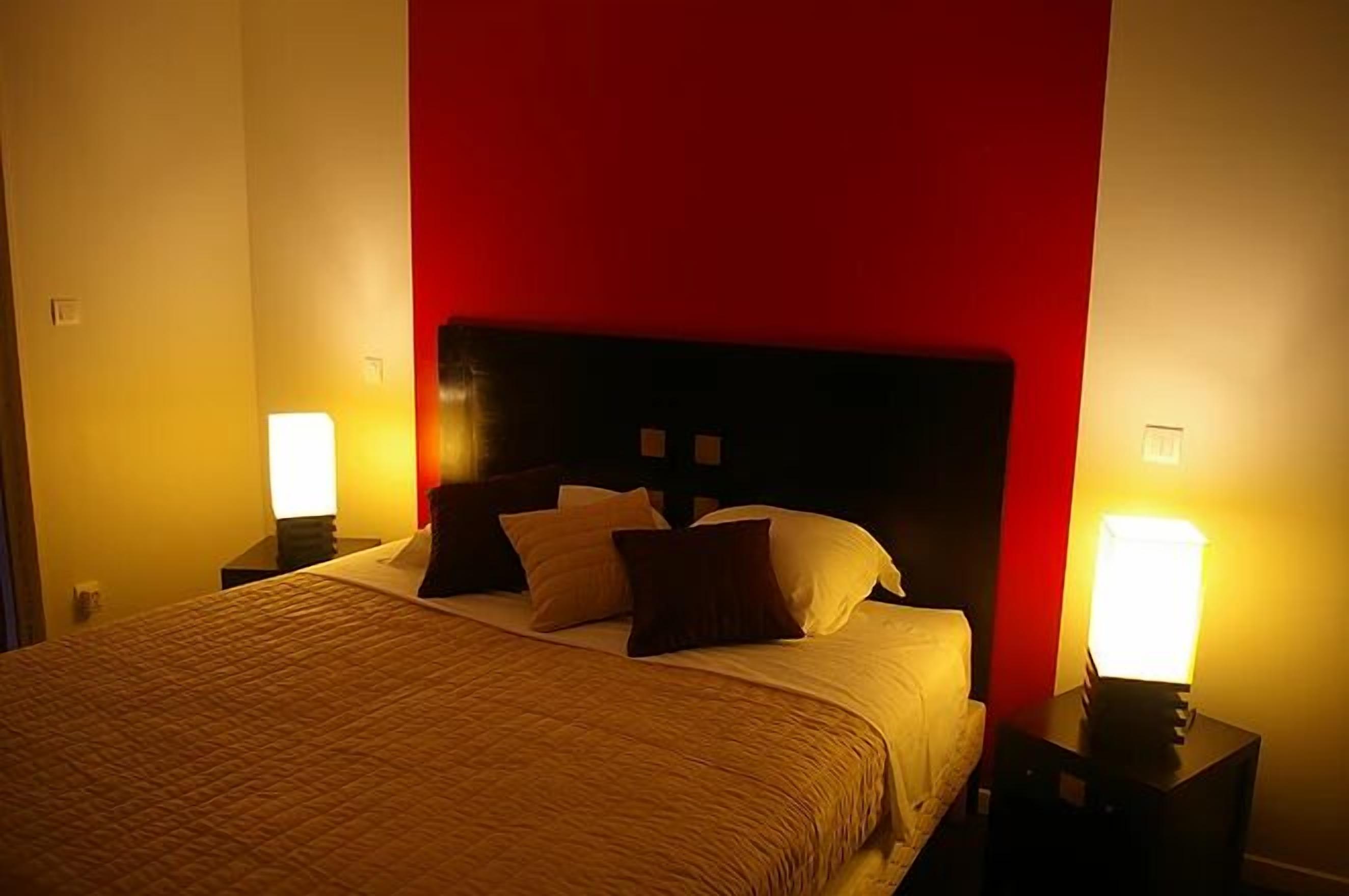 A hotel room with a bed, two bedside lamps, and a red accent wall.