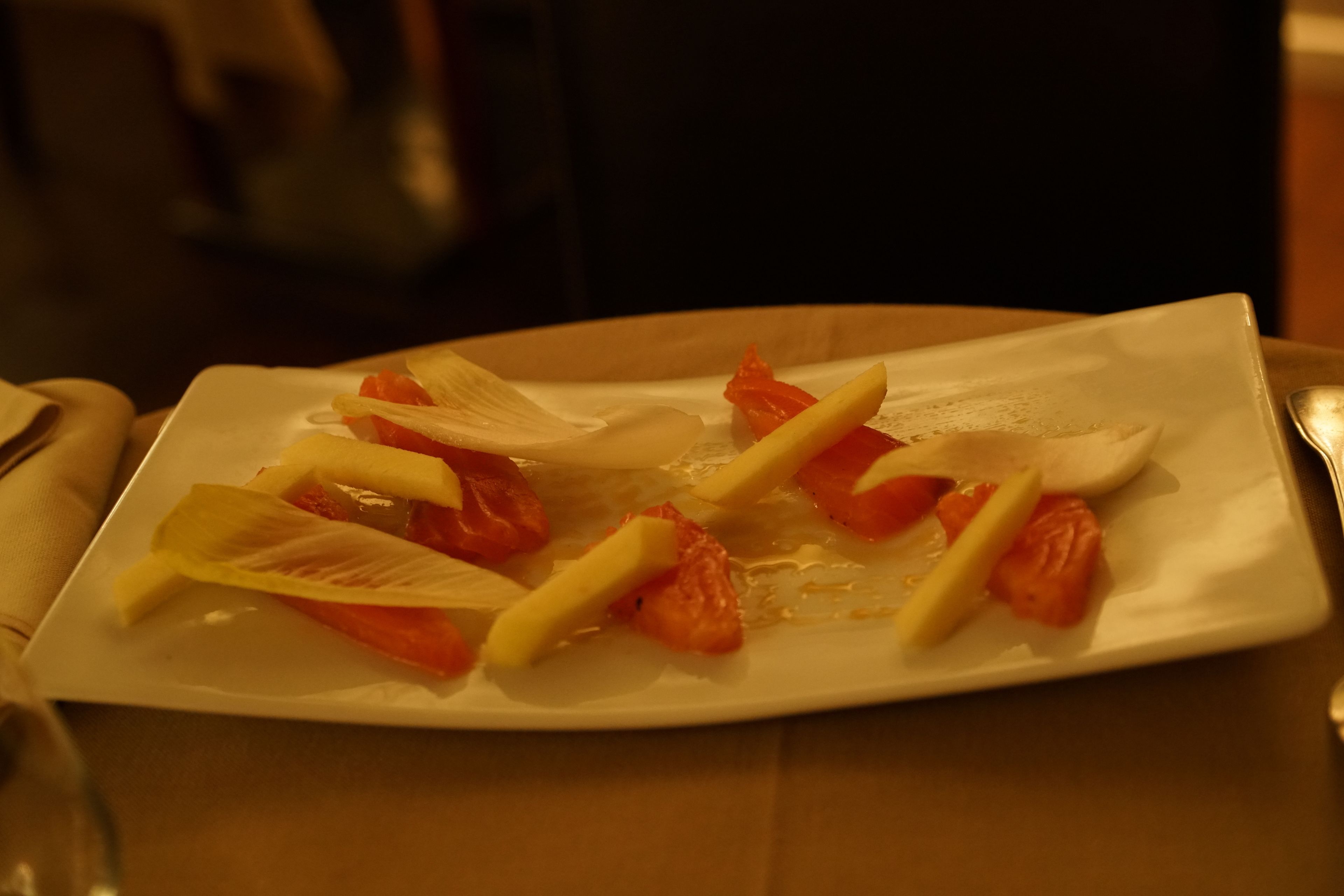 Un plato blanco rectangular con frutas cortadas y una servilleta blanca sobre una mesa de madera.