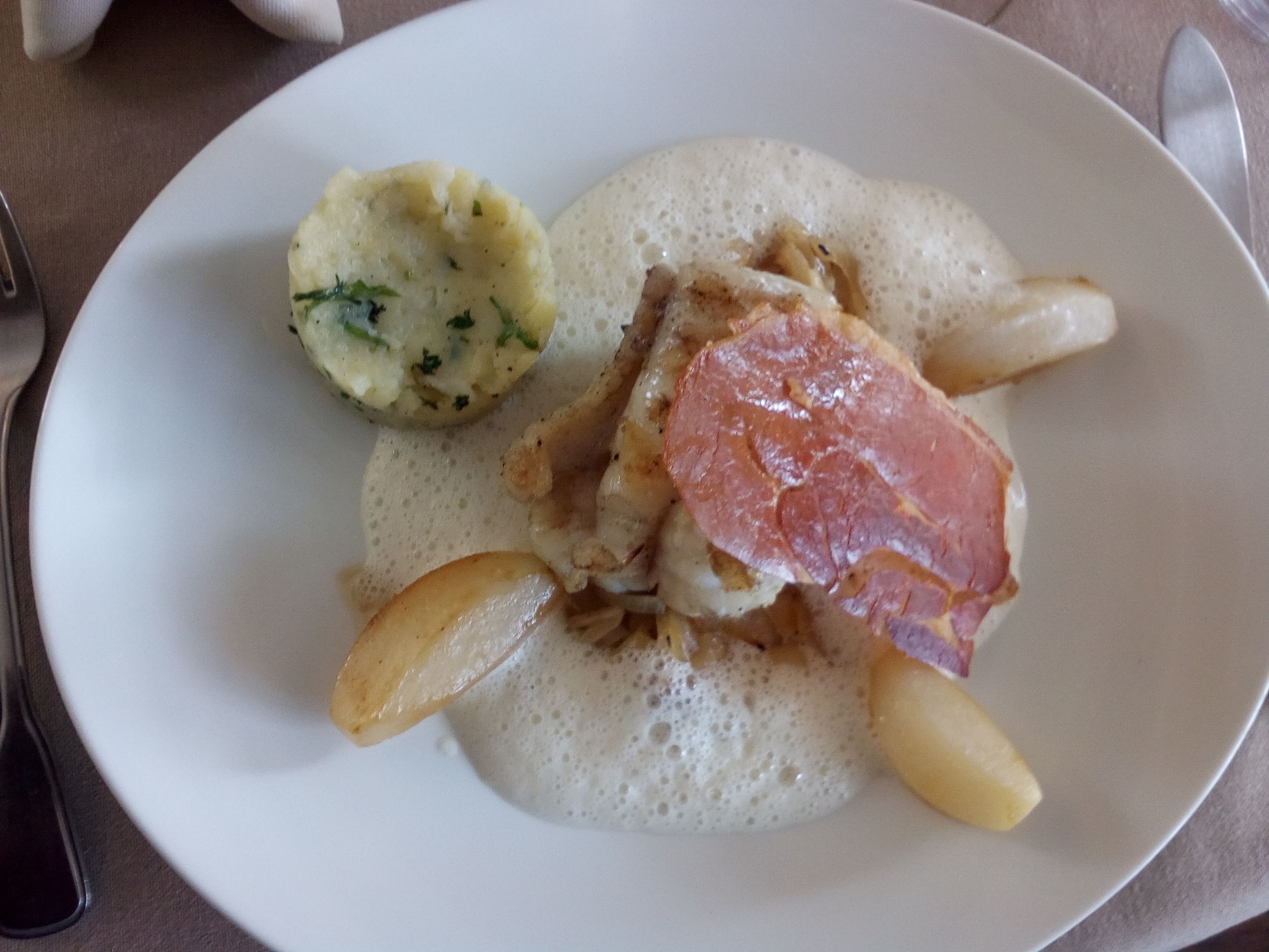 Une assiette contenant un morceau de viande, une pomme de terre et une sauce crémeuse.