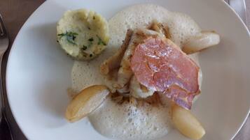 Une assiette contenant un morceau de viande, une pomme de terre et une sauce crémeuse.