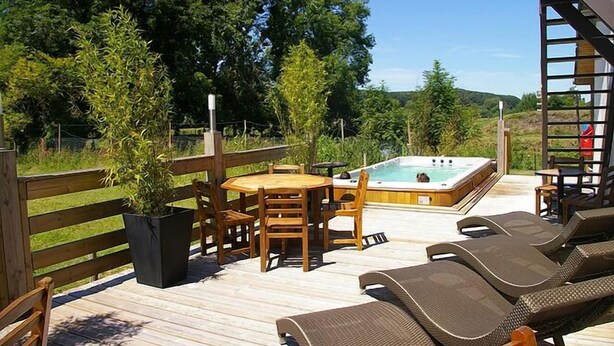 Una terraza de madera con un jacuzzi, sillones de descanso y una mesa con sillas.