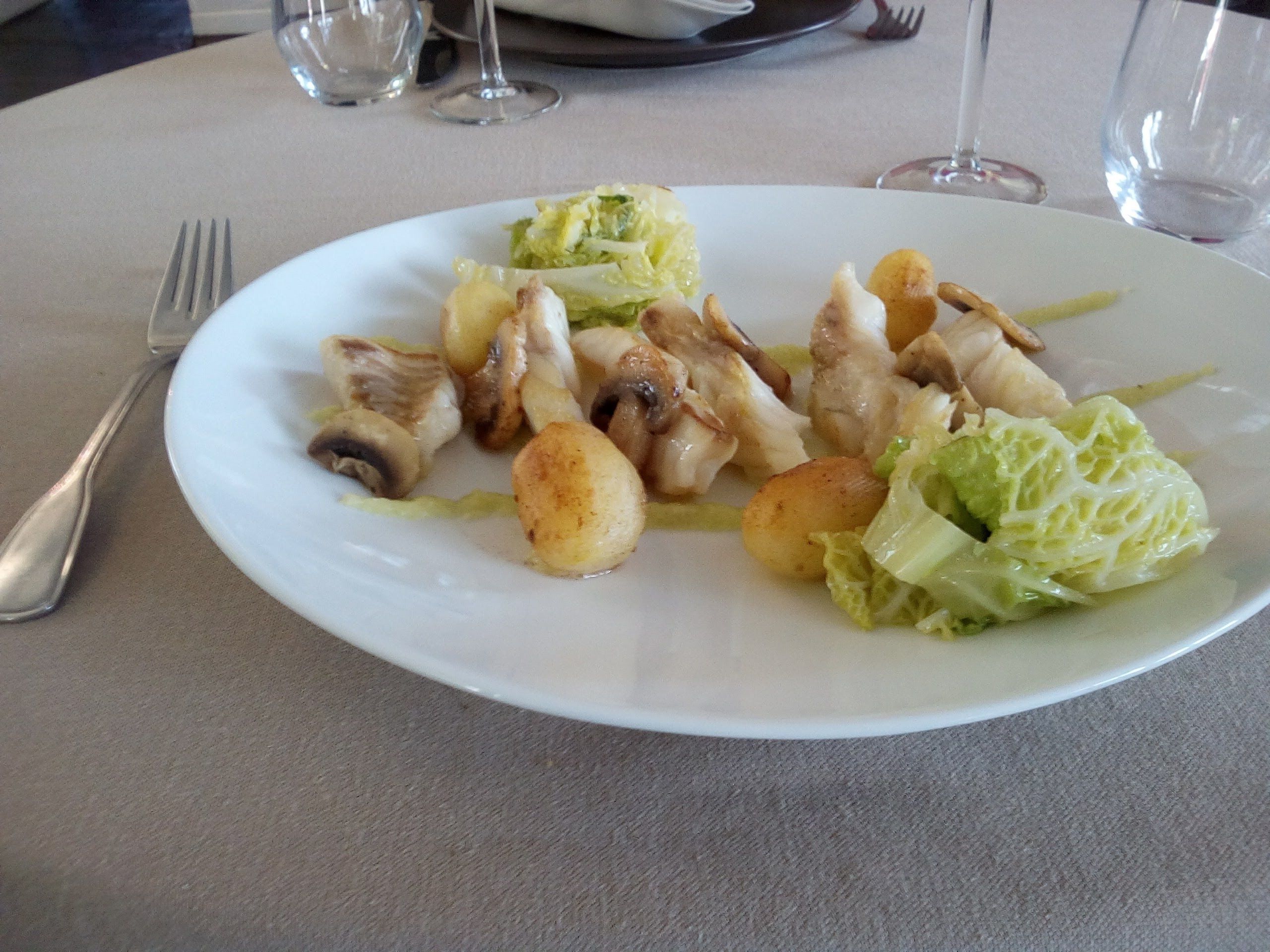 A plate of food with mushrooms, potatoes, and cabbage on a table.