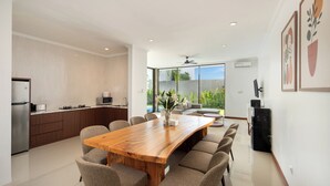 A modern kitchen with a wooden dining table and chairs, a built-in oven, and a large window offering a view of greenery. - Daha Mansions Seminyak (Seminyak)
