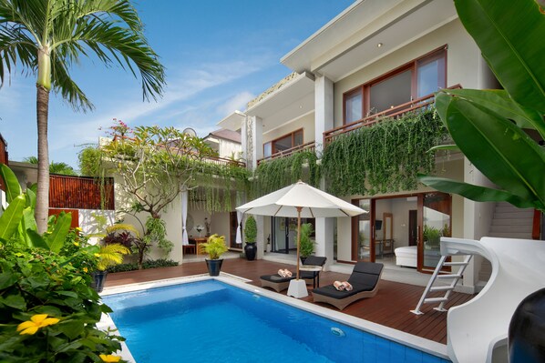 A modern poolside area with a clear blue pool, lounge chairs, and a covered seating area.