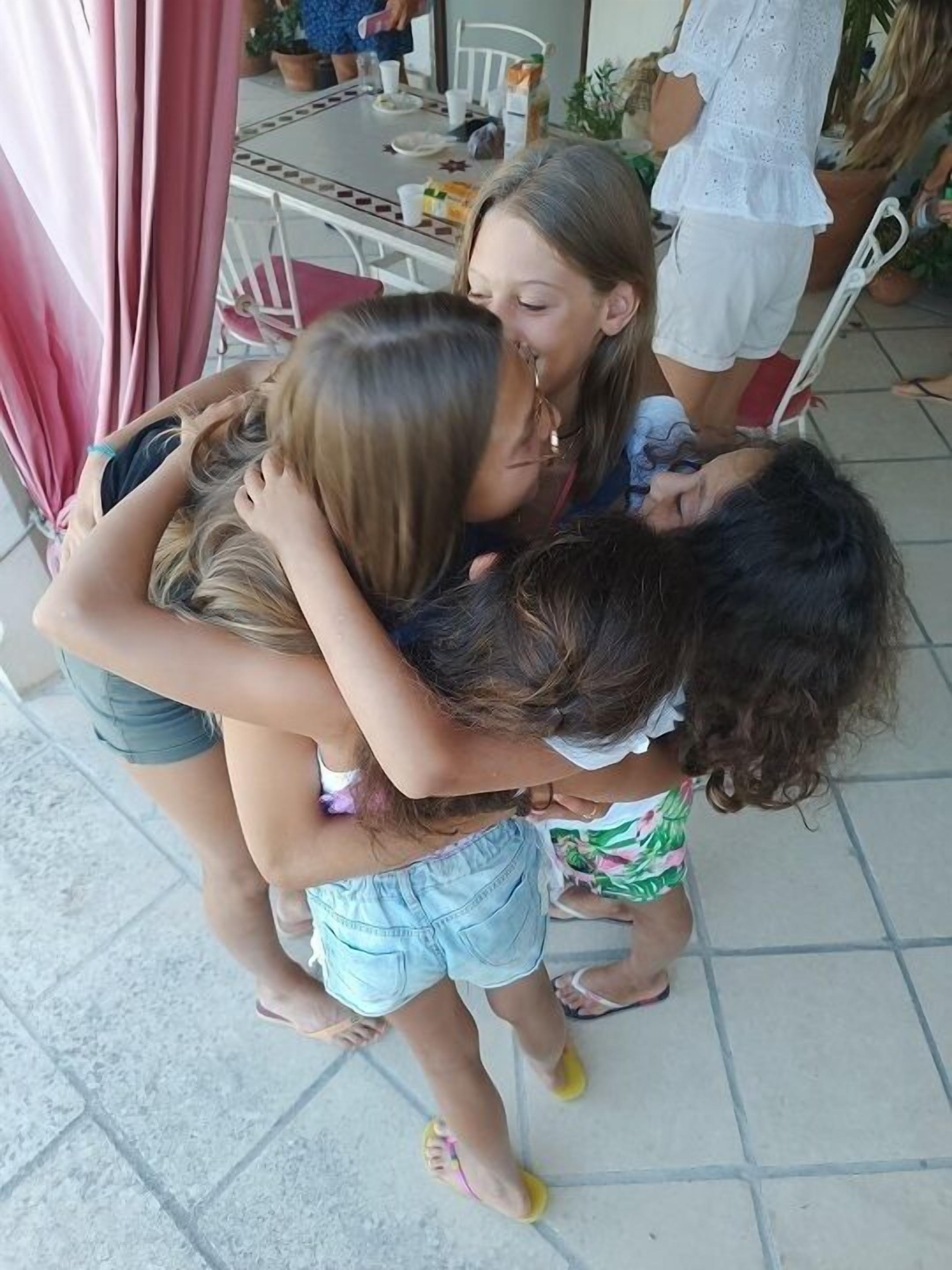 A group of people hugging in a courtyard with a tiled floor and a table with various items on it.