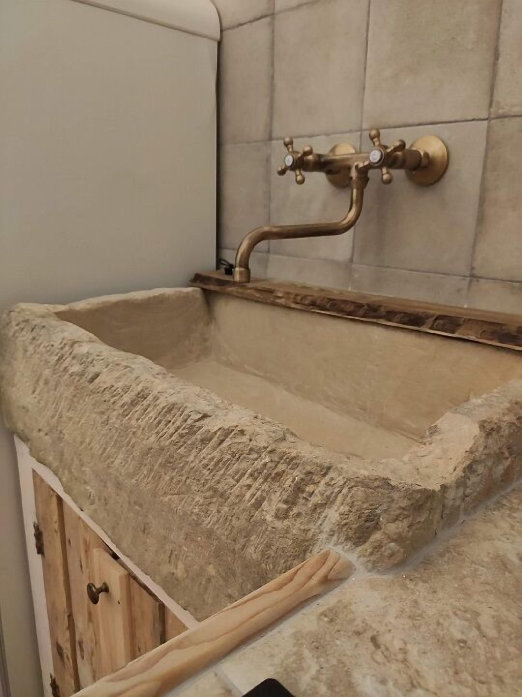 A bathroom with a stone sink, a brass faucet, and a tiled wall.