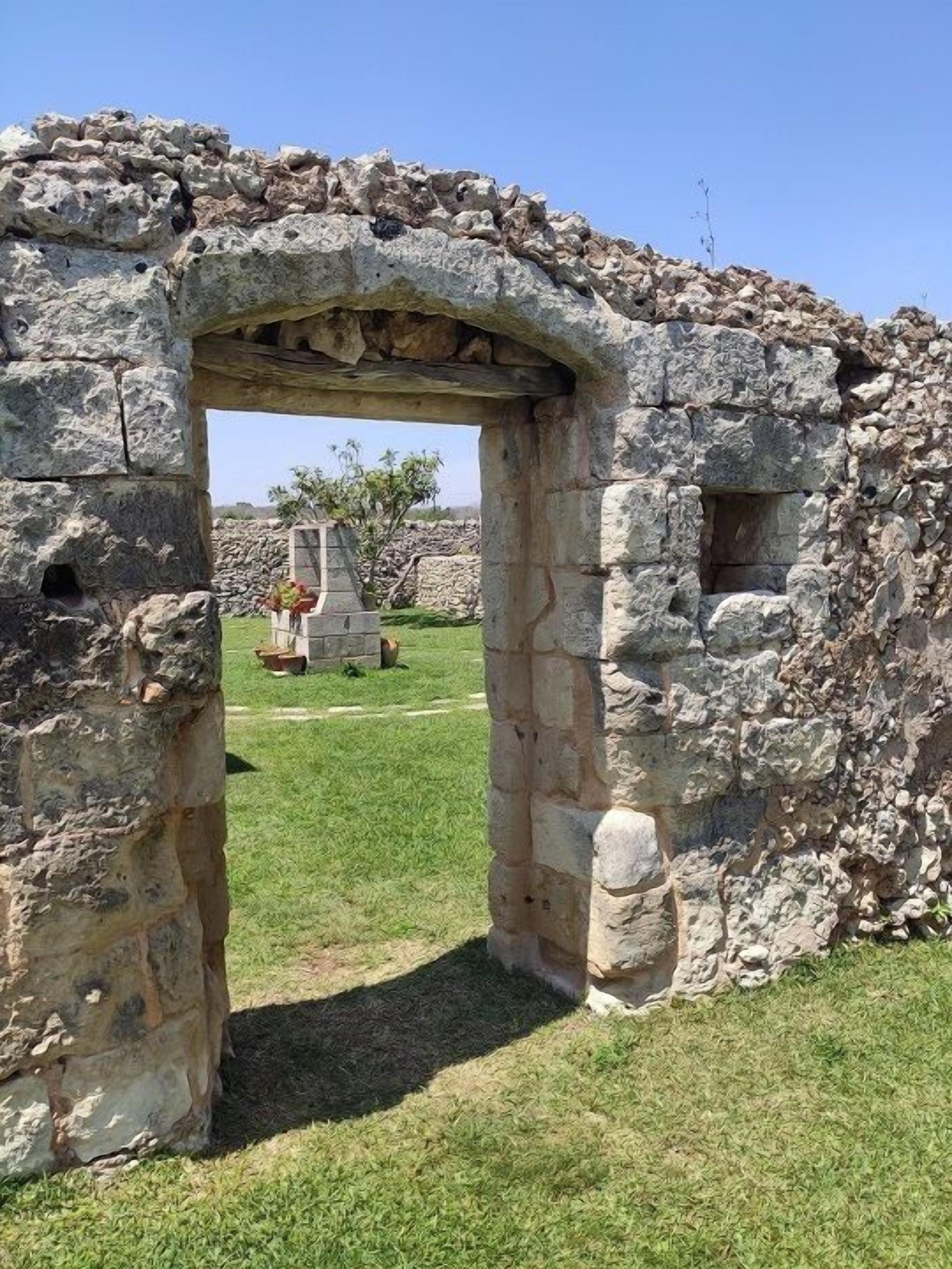 An ancient stone structure with an archway leading into a grassy area.