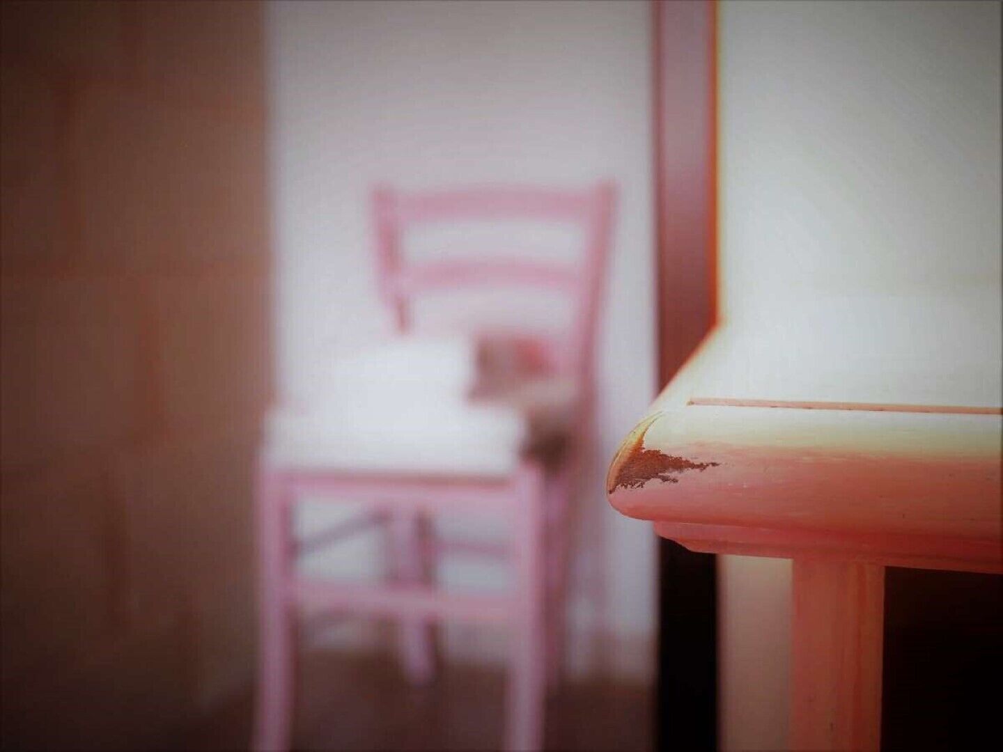 Un gros plan d’une chaise avec une structure rose et un siège blanc, placée dans une pièce dont le mur du fond est uni.