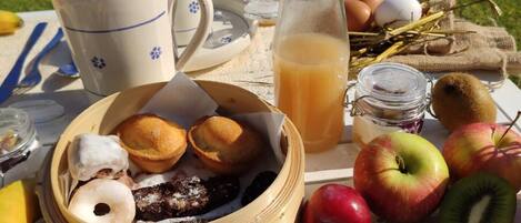 A picnic setup with food items, including a basket of pastries, fruits, and a glass of juice on a table outdoors.