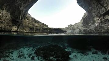 Boca natural de cueva con vista a una masa de agua tranquila y formaciones rocosas.