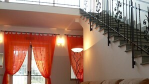 A living room with a sofa, a rug, and a staircase with a wrought iron railing. - Agriturismo Il casale delle Ginestre (Fiumicino)