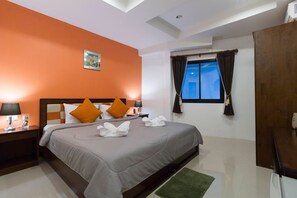 A hotel room with a large bed, orange walls, a window with curtains, and a small table with a lamp. - Samed Big Tree (Rayong)