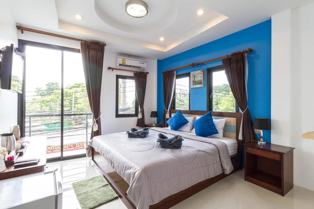 Habitación de hotel con una cama grande, un escritorio con silla, televisor montado en la pared y un balcón con cortinas.