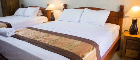 A hotel room with two beds, each with white linens and brown headboards. There are bedside tables with lamps and a wooden wardrobe.