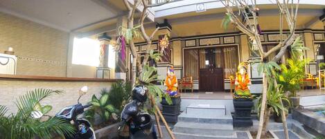 A hotel lobby with a central staircase, potted plants, and two parked scooters.