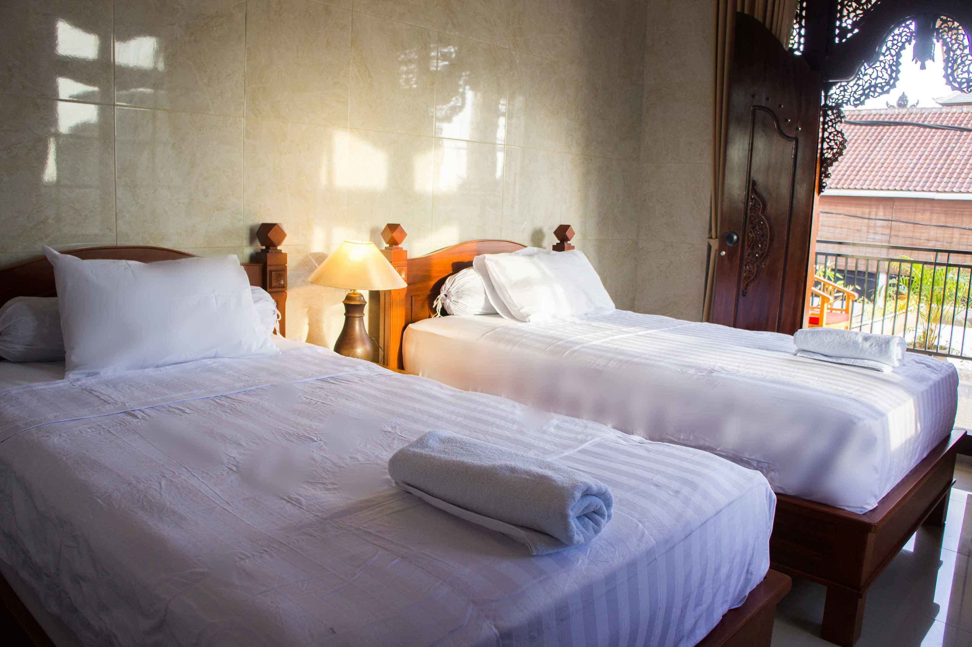 A hotel room with two beds, a nightstand with a lamp, and a view of the outside balcony.