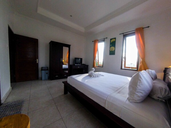 A hotel room with a bed, a desk, a wardrobe, and two windows with curtains.