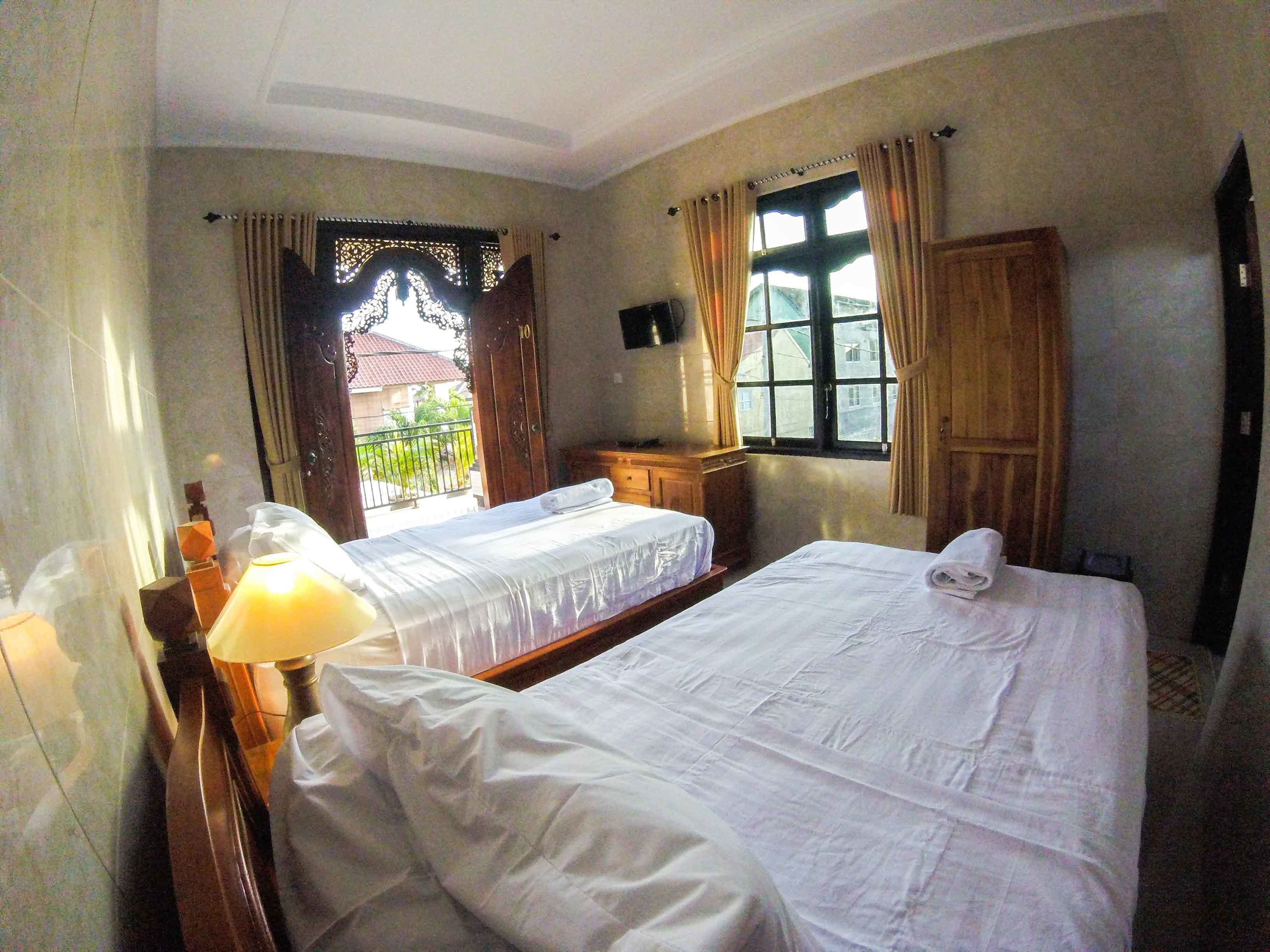A hotel room with two beds, a wooden wardrobe, a desk, and a window with curtains.